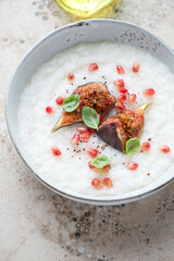 Bowl of rice porridge served with fresh torn figs and pomegranate seeds, vertical shot on a beige granite surface, middle close-up