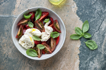 Italian caprese with buffalo mozzarella and heirloom tomatoes, above view on a beige and grey granite background, horizontal shot with space