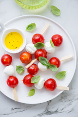 Caprese skewers with mini mozzarella balls, cherry tomatoes and basil on a white plate, vertical shot, flat lay, middle close-up