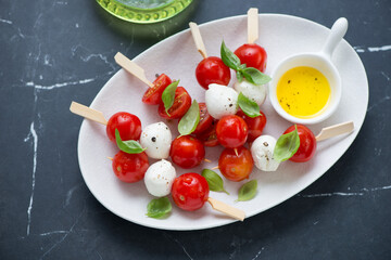 White plate with caprese skewers on a black marble background, horizontal shot, high angle view