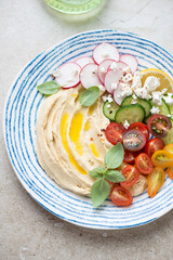 Mediterranean hummus plate with fresh sliced vegetables, vertical shot on a beige stone background, middle close-up