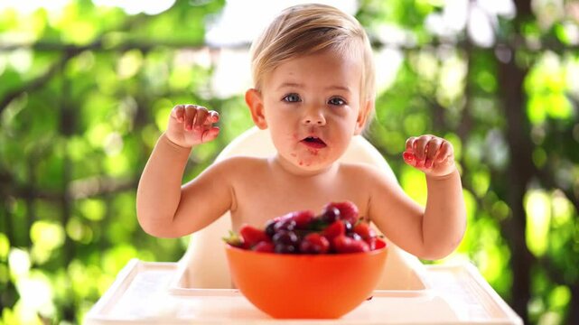 Little girl with a dirty face sits on a high chair and eats a ripe cherry. High quality 4k footage