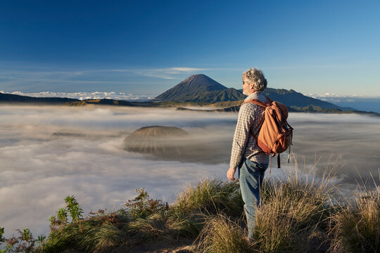 Asia, Indonesia, Java, Bromo Semeru national park, mature male tourist trekking at mount Bromo at sunrise, standing at viewpoint admiring view

