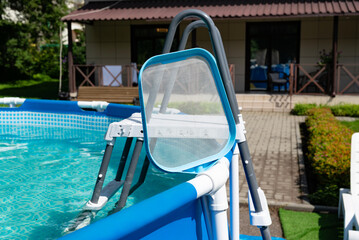 Backyard pool with a cleaning net and ladder near a house on a sunny day.