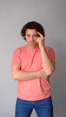 Man shows thinking gesture touching head by finger on gray background. Middle aged curly guy posing feeling misunderstanding. Emotional reaction of male, sincere emotions. Wearing jeans, pink t-shirt.