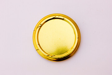 A gold-colored metal plate, circular in shape on a white background. This is the lid of a jam jar photographed from above.