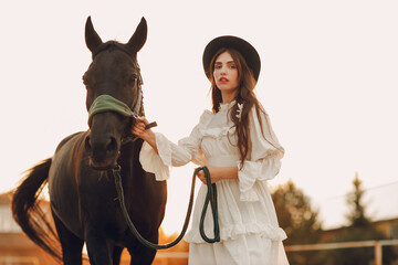 Woman in white dress and black hat with her horse at outdoors ranch