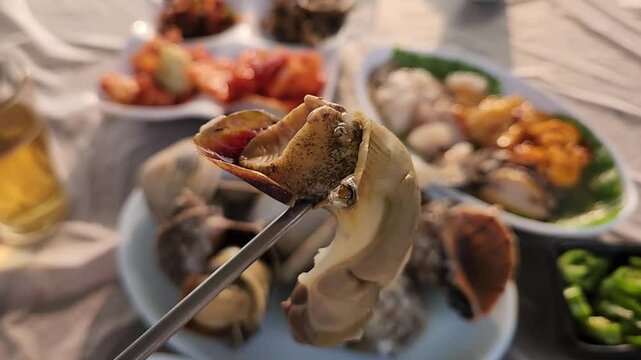 한국의 서해안 바닷가의 식당에서 소라 껍질에서 속살을 발라내는 여자의 손과 쇠 젓가락