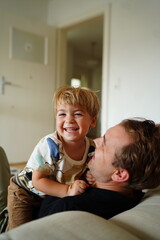 A smiling young boy sitting on his father's lap, both sharing a joyful and playful moment together...