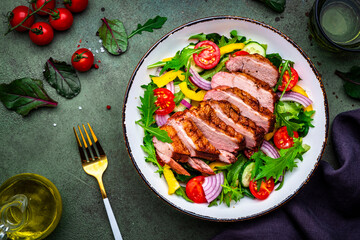 Salad with grilled duck, lettuce and colorful vegetables, green background, top view