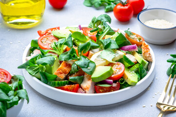 Fresh salad with avocado, chicken, tomatoes and lettuce, gray background, top view