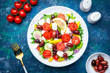 Traditional greek salad with feta cheese, kalamata olives, tomatoes, paprika, cucumber and onion, healthy mediterranean diet food. Blue table background, top view