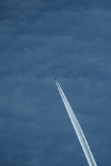 Airplane in the blue sky with contrail in the clouds.