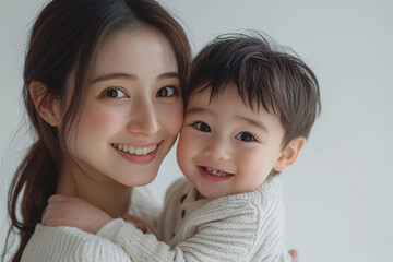 Young Japanese mother holding her cute young son, both looking into the camera, in front of a white studio background, showcasing a tender moment of family bonding and love