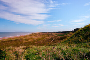 Fototapeta premium Danish Coastal Landscape. Hilly coast of the northern sea. Sun, blue sky, clouds, waves and grass. Beautiful landscape summer on the northern sea