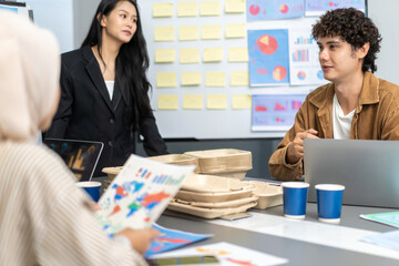 Diverse team of business professionals discussing global market trends and data during a corporate strategy meeting with charts, eco-friendly packaging, and visual aids for sustainable development