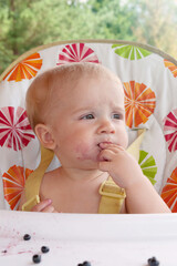 The child licks his fingers with pleasure after eating blueberries