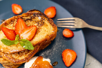 French toast garnished with strawberries and mint, with ice cream and caramel sauce on a blue plate. Delicious and healthy breakfast. Close-up