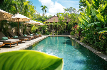 the swimming pool area in an elegant Balinese-style villa with lush greenery and comfortable loungers along its edge, surrounded by vibrant tropical plants.