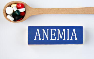 ANEMIA - word on a wooden blue block on a white background with a spoon with pills in the background