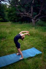 little 5-year-old girl in a black minimalist overall does gymnastics in the garden, outdoors