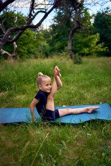 little 5-year-old girl in a black minimalist overall does gymnastics in the garden, outdoors