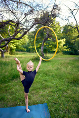 little 5-year-old gymnast in a black minimalistic leotard exercises with a hoop in the garden