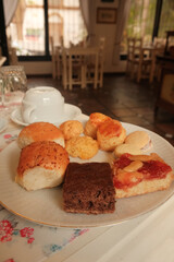 Close up of plate of sweet pastries and bakes on white breakfast plate, in dining room of hotel, hostel stay or guesthouse in Colonia del Sacramento, Uruguay. Rustic cozy mood