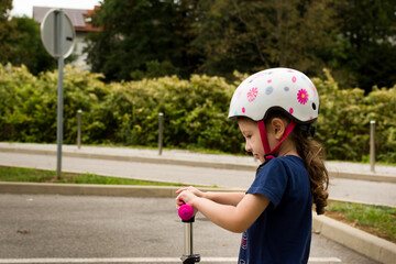 Close up of little girl wearing helmet on scooter, with green vegetation as background