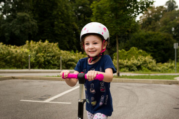 Happy little girl wearing helmet on scooter, with green vegetation as background