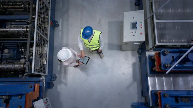 Worker consulting with a woman manager in the factory, analyzing graphs and data on a tablet to improve production processes, top down shot.