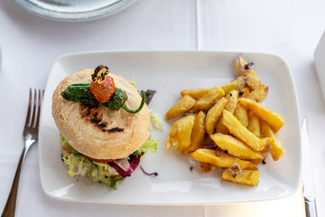 Veganer Burger, auf einem weißen Teller mit Pommes Frites und im Restaurant