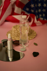 straw hat, sunglasses, bottle of water, sunscreen spray, american flag on colored background