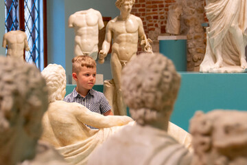 Young boy observing with interest sculptures exhibition in art museum, pointing to something interesting. High quality photo