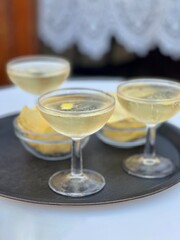 Three cocktails on a bar tray with potato chips or crips.  Taken at an outdoor bar.   