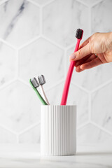 Hand of woman reaches for toothbrush standing in holder