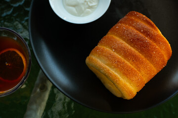 Kurtoskalacs, hungarian sweet chimney cake on a black plate. Served as a breakfast alongside black coffee, in a cafe environment