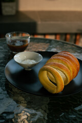 Kurtoskalacs, hungarian sweet chimney cake on a black plate. Served as a breakfast alongside black coffee, in a cafe environment