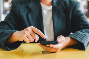 Close-up of a person using a smartphone, wearing a plaid blazer, and touching the screen. Casual and modern setting.