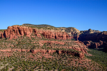 Breathtaking view of Sedona's iconic red rock formations under a clear, vibrant blue sky. Arizona's stunning landscape showcases layered rock structures and lush greenery - USA