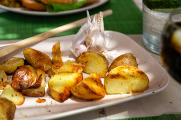 Gebackene Kartoffelecken mit einer Knolle Knoblauch auf der Terrasse unter Sonnenlicht