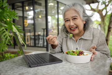 Senior Woman Enjoying a Healthy Salad at a Cafe with Laptop, Surrounded by Greenery and Natural Ligh