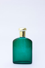 Elegant Green Glass Bottle: A single, empty green glass bottle with a gold-colored cap stands prominently. The translucent green hue of the bottle contrasts beautifully against the plain white backgro