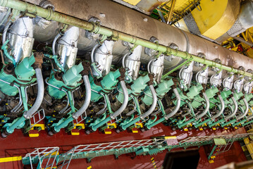 Aerial top view of the main engine on a large container ship, focusing on the cylinder heads with exhaust valves and the oil pipes that control them. 