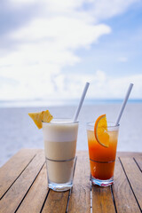 Two delicious chilled cocktails on a wooden table against the backdrop of a seascape. Tasty drinks with straws and slices of citrus fruits. A romantic evening on vacation.