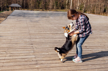 A little girl hugs her corgi puppy on the street. A cute kid in casual clothes is laughing and playing with her dog on a wooden platform.