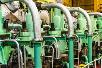 A close-up of the main engine on a large container ship, focusing on the cylinder heads with exhaust valves and the oil pipes that control them. 