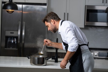 modern chef in professional uniform. close-up on the hand of male chef who is stirring soup in pot with spoon. cooking, culinary and people concept - male chef in toque with pot or saucepan.