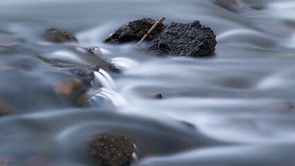 Rocks and wood in creek with silky water, long exposure