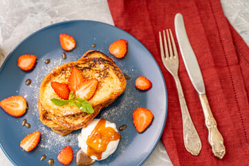 French toast with strawberries and mint, ice cream, drizzled with caramel sauce and orange juice on a blue plate with cutlery on a gray background. Healthy breakfast concept.